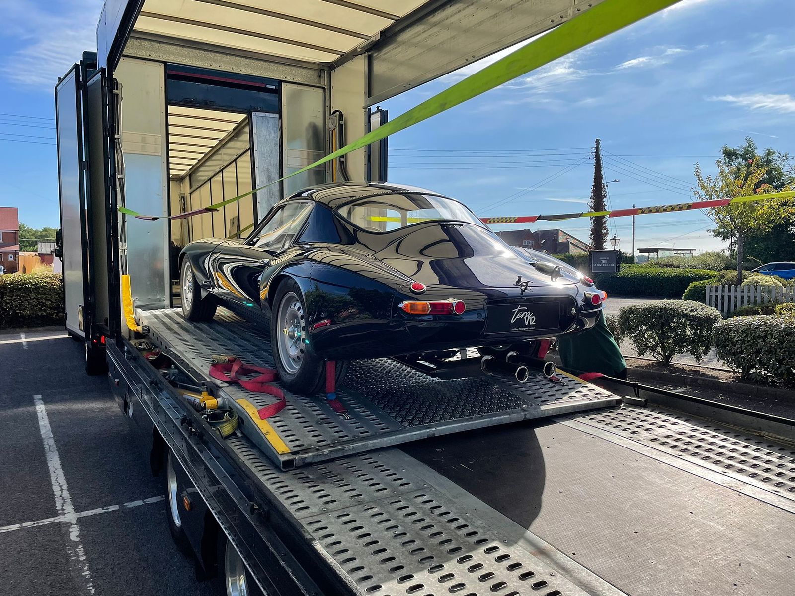 E-Type Re-Imagined — black coupe secured on a transporter